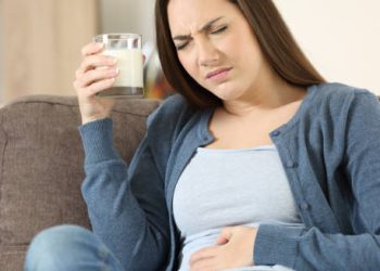 Woman holding a glass of milk and clutching her stomach in discomfort