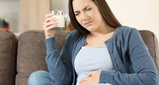 Woman holding a glass of milk and clutching her stomach in discomfort