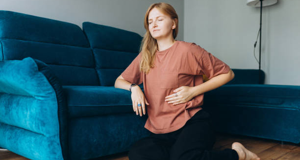 Woman sitting on the floor with her hand on her stomach, showing signs of abdominal discomfort