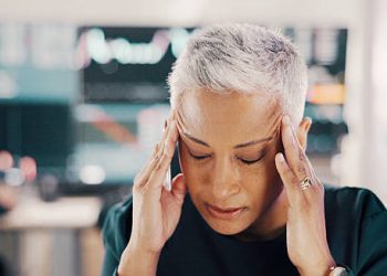 Woman with grey hair touching her temples in pain, showing symptoms of Giant Cell Arteritis