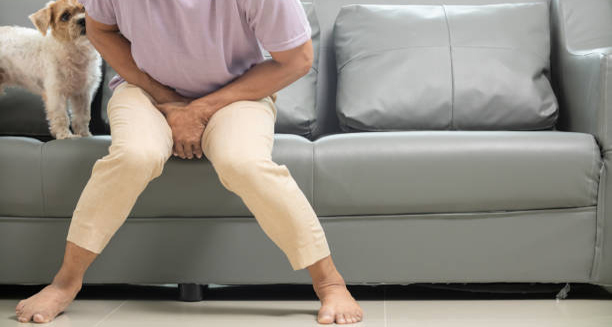 Man sitting on couch showing pelvic discomfort, possibly indicating STI symptoms