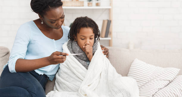 Mother checking the temperature of a sick child wrapped in a blanket.