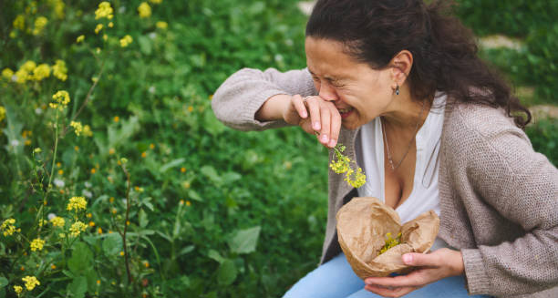 Woman sneezing outdoors while holding wildflowers, showing allergic hay fever symptoms
