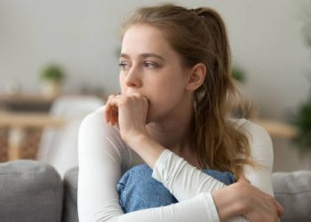 Anxious young woman sitting on a couch, looking worried and lost in thought