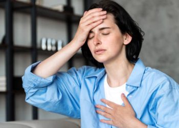 Woman holding her head and chest with eyes closed, showing dizziness and discomfort from heart block