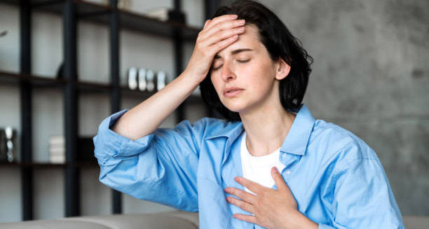 Woman holding her head and chest with eyes closed, showing dizziness and discomfort from heart block