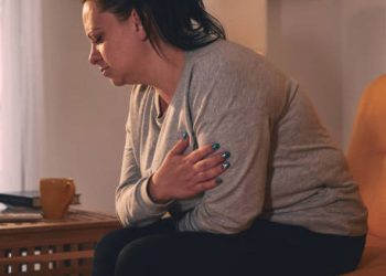 Woman in visible discomfort clutching her abdomen and chest during a heavy period