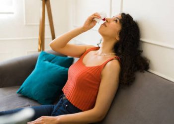 Woman using tissue for nosebleed while sitting on couch