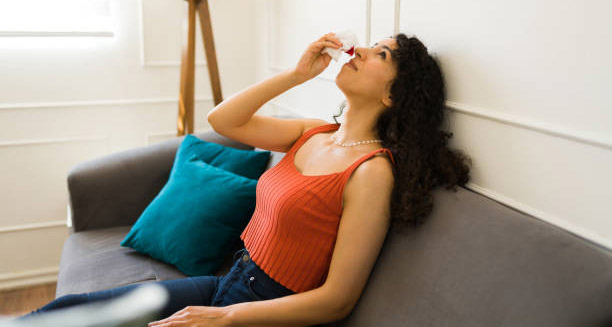 Woman using tissue for nosebleed while sitting on couch