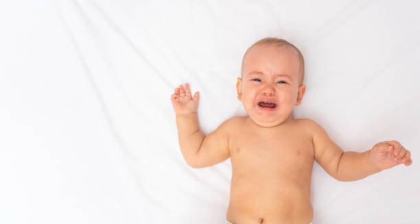 Crying baby lying on white sheet, indicating possible symptoms of Hirschsprung’s disease