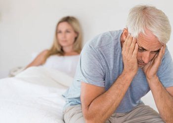 Older man sitting on bed with head in hands, showing symptoms of impotence