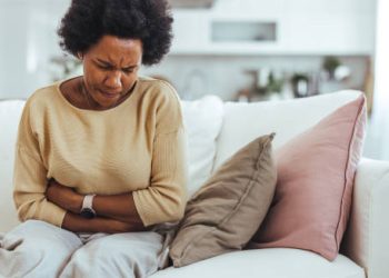 Woman clutching her stomach in pain while sitting on a couch, showing IBS symptoms