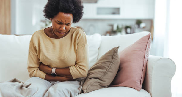 Woman clutching her stomach in pain while sitting on a couch, showing IBS symptoms