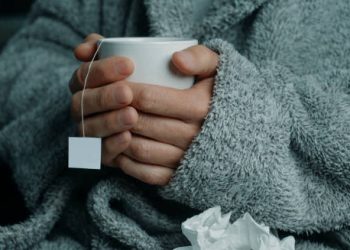 Person in robe holding tea cup as flu treatment