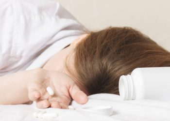 Person lying on bed with spilled pills and an open medication bottle, depicting severe food poisoning treatment
