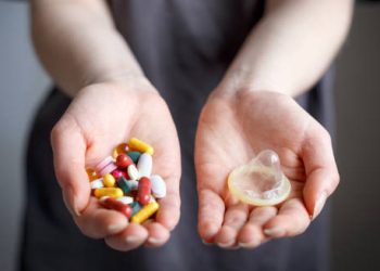 Hands holding antiviral pills and a condom for genital herpes treatment