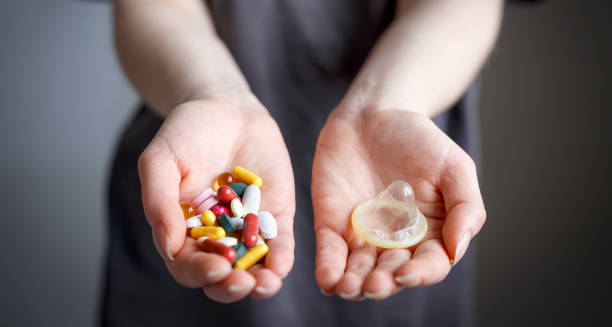 Hands holding antiviral pills and a condom for genital herpes treatment