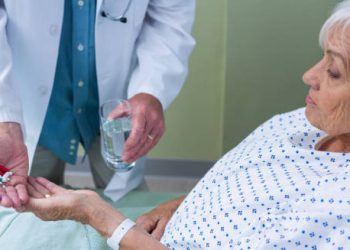 Doctor giving medication and water to elderly patient in hospital bed