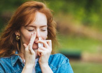 Woman using nasal spray outdoors to treat hay fever symptoms