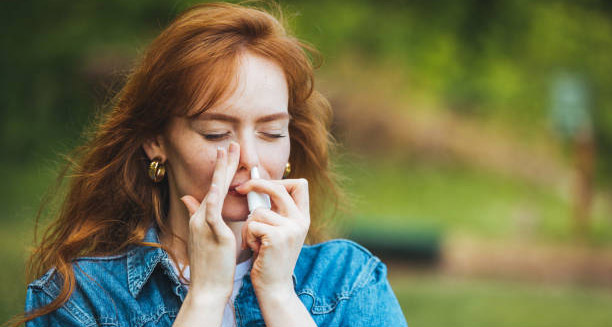 Woman using nasal spray outdoors to treat hay fever symptoms