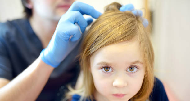 Doctor wearing gloves examining young girl’s hair for lice treatment