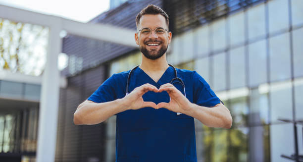 Smiling male doctor in scrubs forming a heart shape with hands, symbolising heart health and treatment