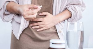 Woman taking medication for inflammatory bowel disease with hand on stomach