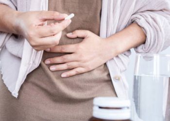 Woman taking medication for inflammatory bowel disease with hand on stomach