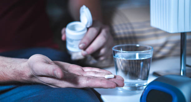 Person taking a sleeping pill with a glass of water at night