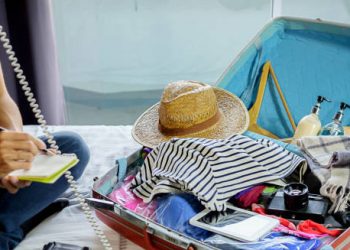 Open suitcase with travel essentials and person making notes, preparing to manage jet lag