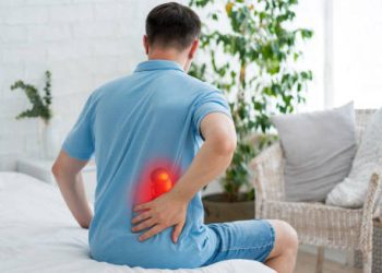 Man sitting on bed holding lower back in pain due to kidney infection complications