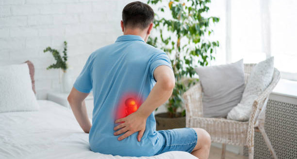 Man sitting on bed holding lower back in pain due to kidney infection complications